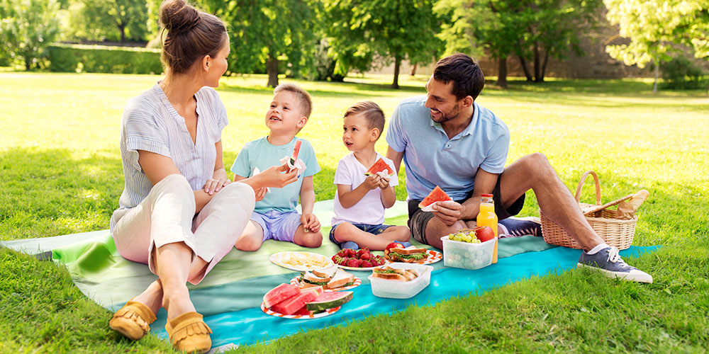 Familie mit 2 Kindern sitzt auf einer Outdoor-Decke und macht Picknick