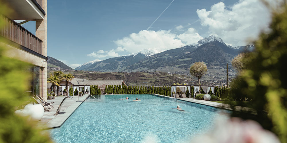 Menschen schwimmen im Hotel-Infinity-Pool und genießen dabei den Panoramaausblick auf die Stadt Meran in Südtirol in den Alpen i